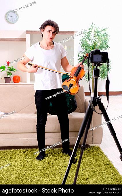 Young male blogger playing violin at home