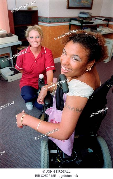 Young woman with cerebral palsy using wheelchair, smiling with carer
