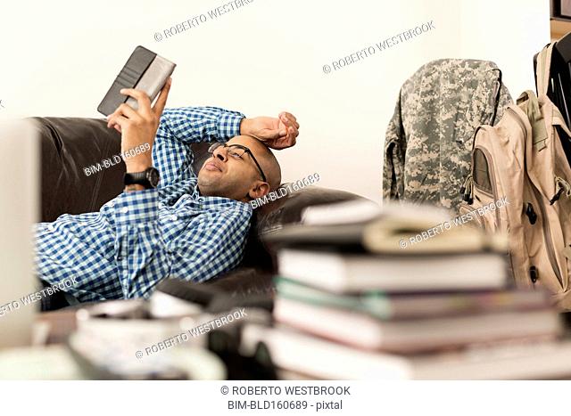 Mixed race man using digital tablet on sofa near books