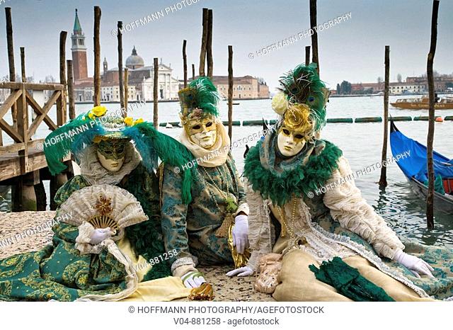 A group of masked persons at the carnival in Venice sitting at the pier in front of San Giorgio Maggiore in Venice, Italy, Europe