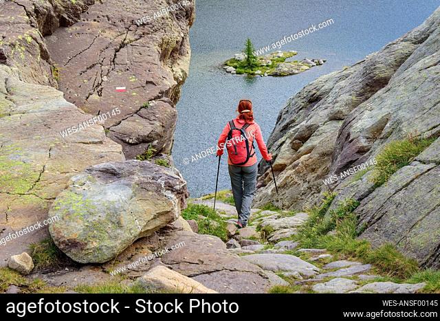 Woman with backpack and hiking poles walking towards Lac Fourca lake, Maritime Alps, Mercantour National Park, France