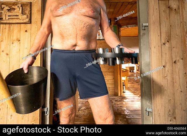 Copenhagen, Denmark A man in shorts stands with a bucket and a tray of scents in front of a wooden sauna