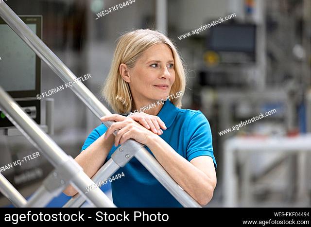 Blond female professional contemplating while standing at railing in factory