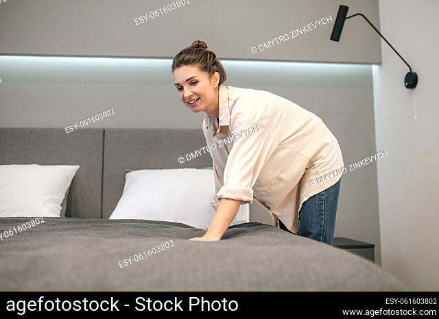 Making bed. A young woman making bed and looking positive