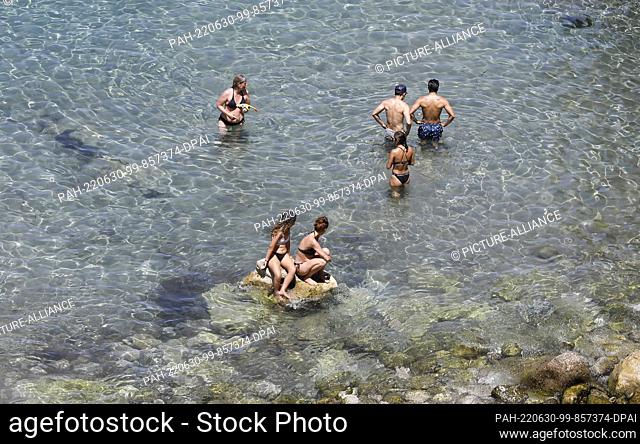 29 June 2022, Spain, Deia: Tourists sunbathing and swimming at the rocky beach Cala Deia in Mallorca. Photo: Clara Margais/dpa. - Deia/Mallorca/Spain