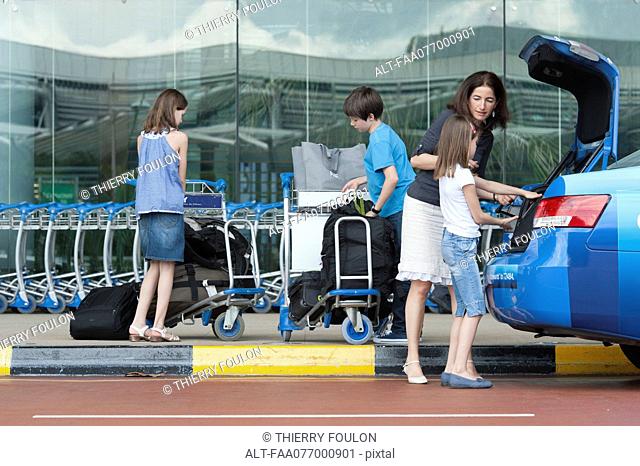 Family outside of airport unloading luggage from taxi trunk