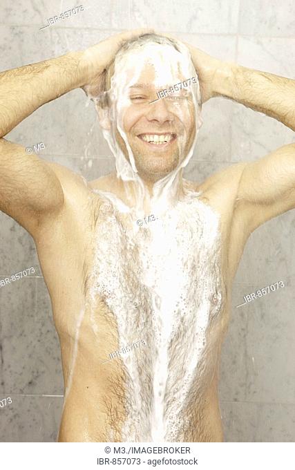 A man with chest hair is having a shower and using a lot of shampoo