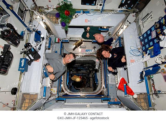 Three of the six crew members aboard the International Space Station peek out of their sleeping quarters on Christmas morning to view the station's decorations...