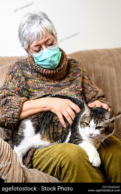 Coronavirus social distancing due to pandemic outbreak. Elderly Woman with protective face mask, Staying At Home stroking her Cat