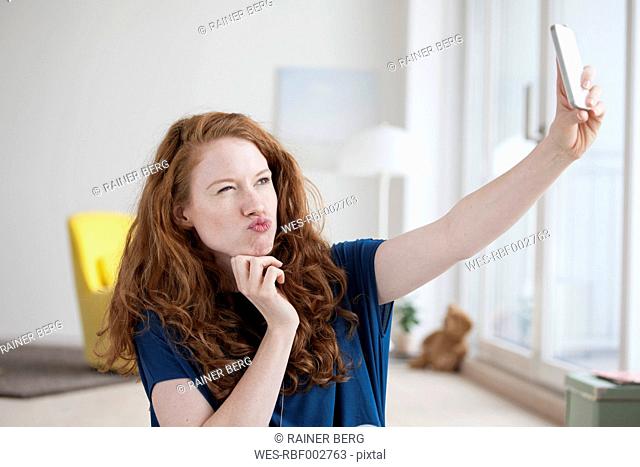 Young woman sitting in her living room taking a selfie with smartphone