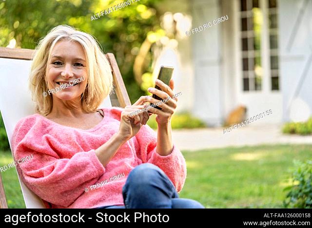 Portrait of smiling mature woman using smartphone while sitting on deckchair