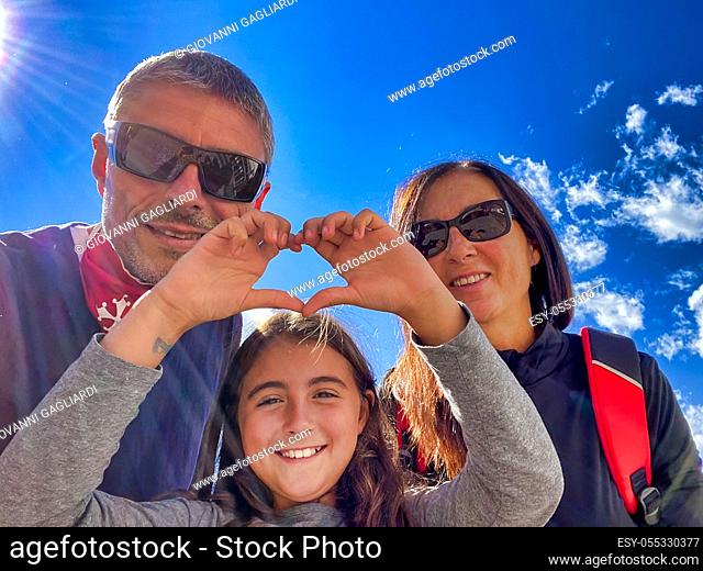 Family of three people on a mountain trail with young girl making heart sign. Holiday concept
