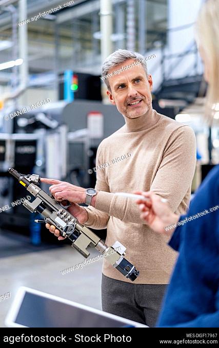 Businessman with device talking to colleague in factory