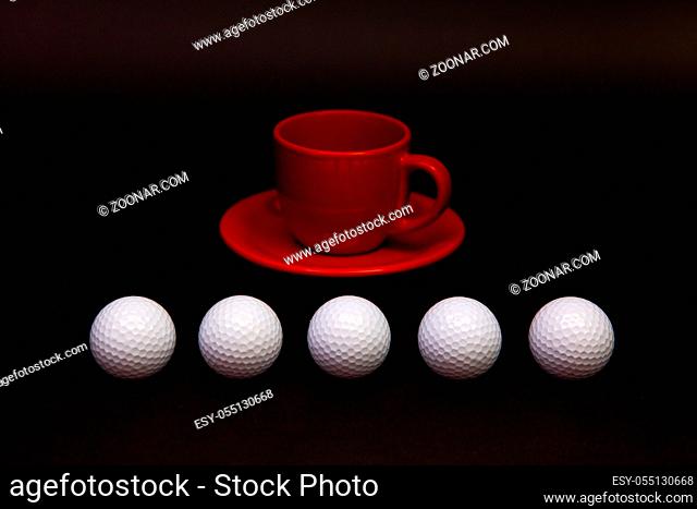 White golf balls and red cup of tea on the black table. White golf ball in front of a black background. Breakfast composition