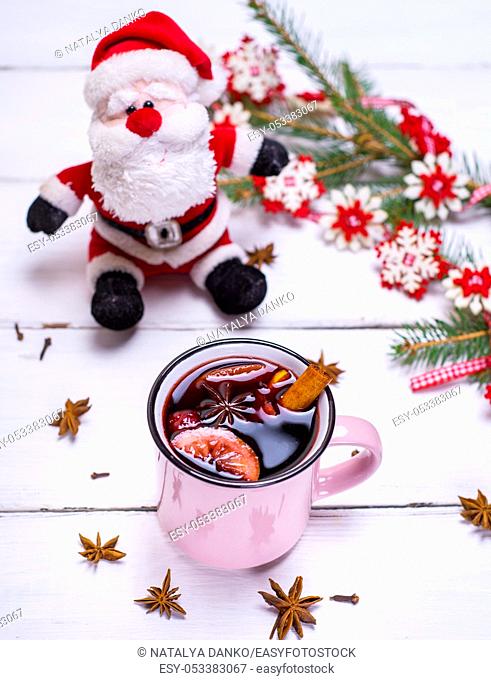 mulled wine in a pink mug on a white wooden background, behind textile santa claus and a spruce branch with a garland