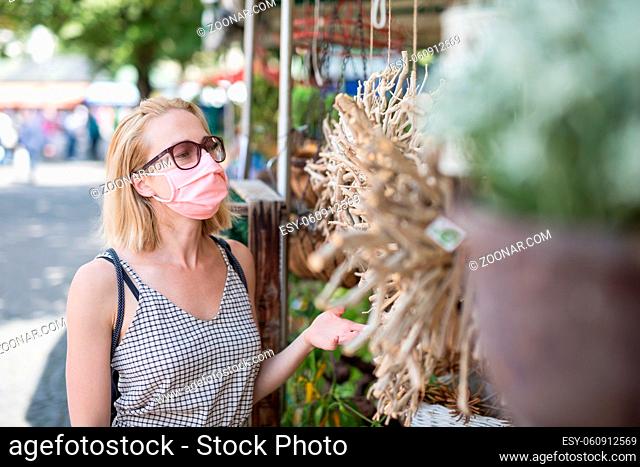 Casual woman shopping for plants outdoor at open market stalls wearing fase masks for protection from corona virus pandemic in Munchen, Germany