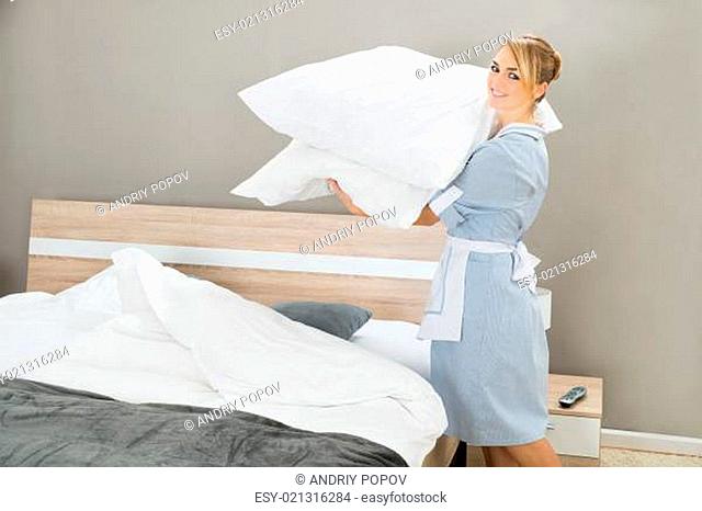 Happy Female Housekeeping Worker With Pillows In Hotel Room