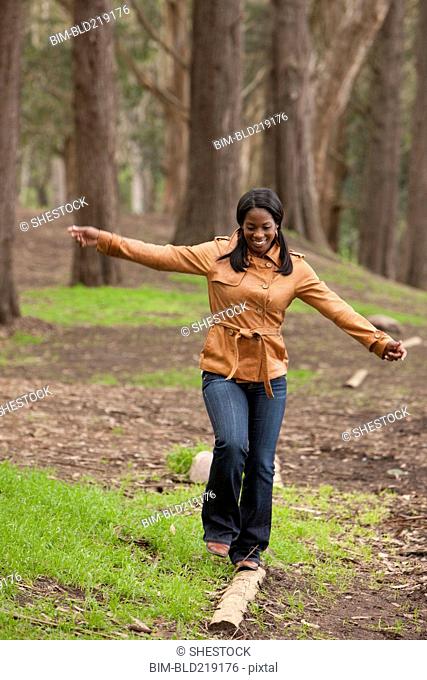 Black woman balancing on log in forest