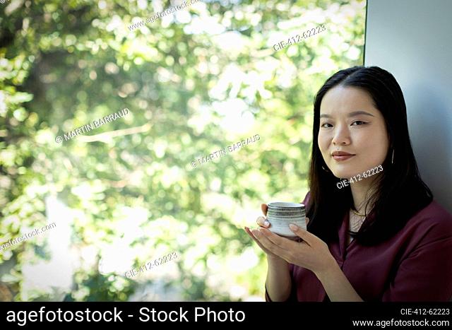 Portrait young woman drinking tea in window