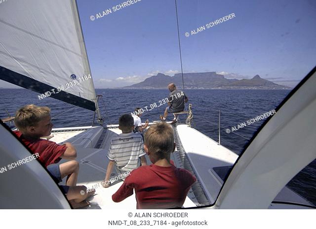 Rear view of two men with three boys on a sailboat, Table Mountain, Cape Town, Western Cape Province, South Africa