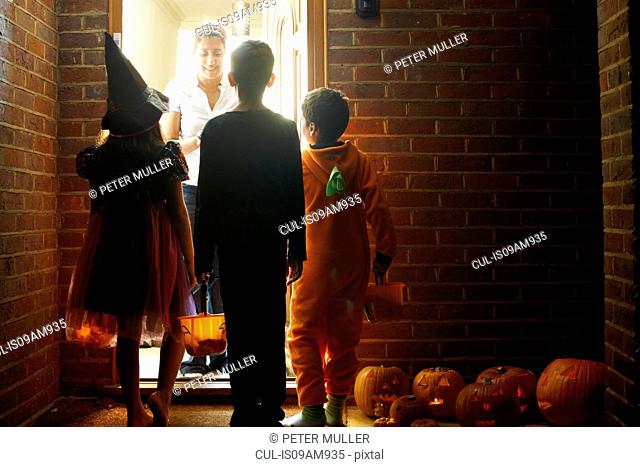 Rear view of three children wearing halloween costumes trick or treating
