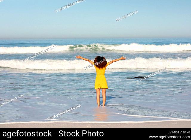 A mixed race woman with her arms outstretched on beach on a sunny day