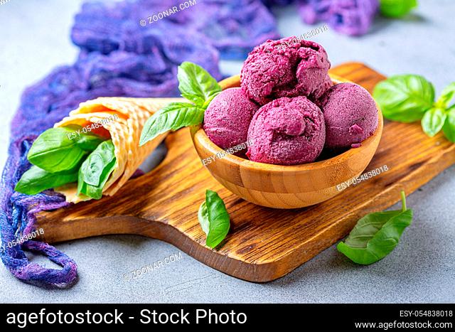 Artisanal blueberry ice cream and green basil in a wooden bowl on a serving board, selective focus