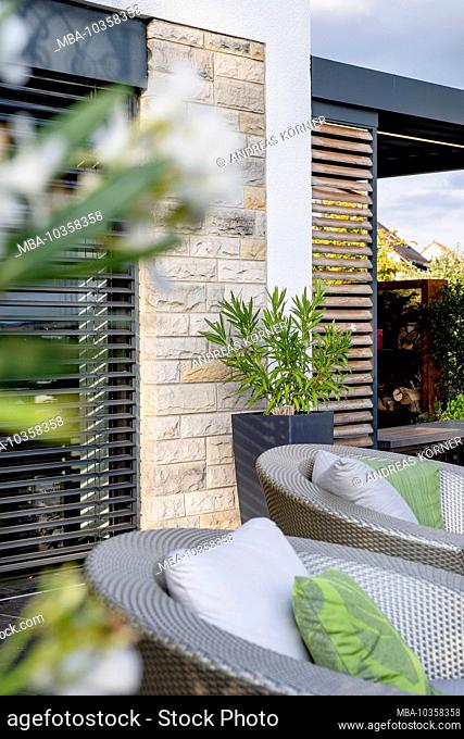 Artificial rattan garden furniture in front of a modern house facade surrounded by branches of orleader