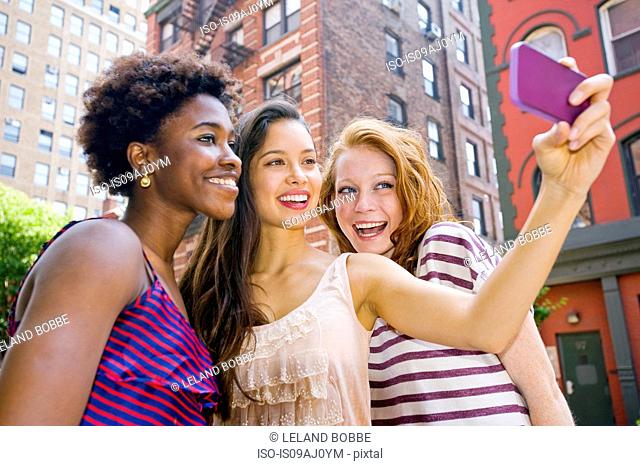 Three young women taking picture of themselves using mobile phone