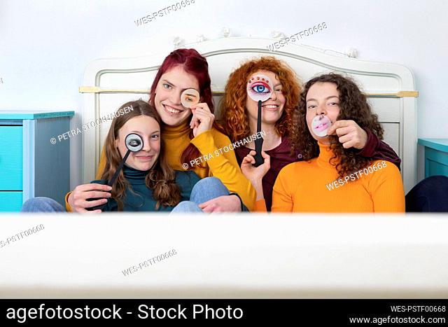 Family portrait of mother and her three daughters sitting together on bed holding paper masks