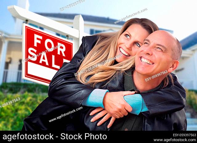 Happy Couple Hugging in Front of For Sale Real Estate Sign and House