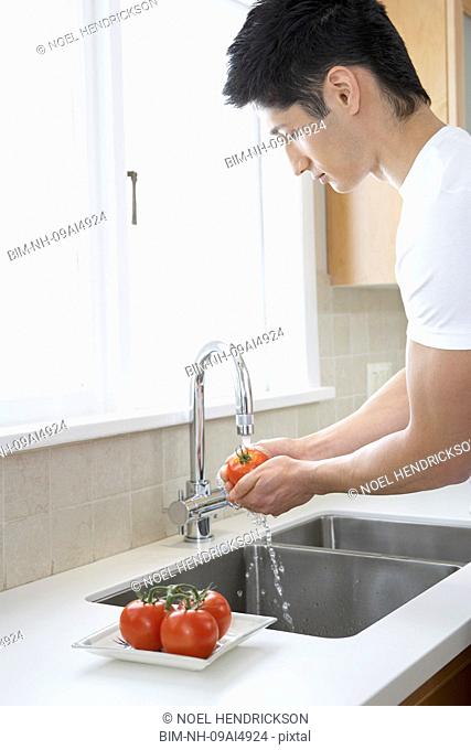 Asian man washing tomatoes in kitchen