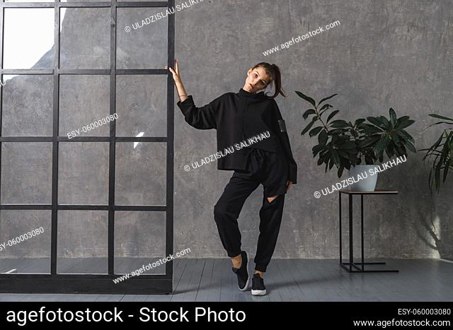 Young woman in black sportswear, pants and sweatshirt. Concept of fashionable sport outfit, indoors photo. Copy space. The concept of sports, healthy lifestyle