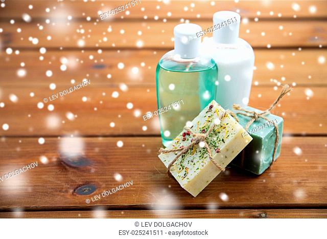 beauty, spa, bodycare, bath and natural cosmetics concept - handmade soap bars and lotion bottles on wooden table over snow