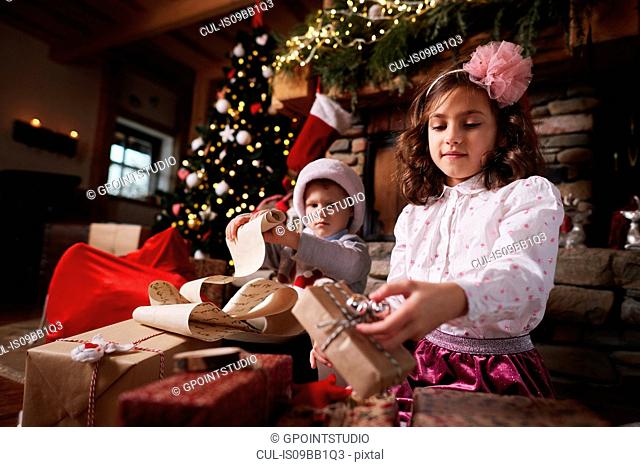 Young girl and boy sorting Christmas gifts, young boy rolling list