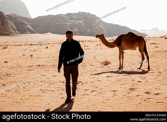 Young man walking in desert with camel in background