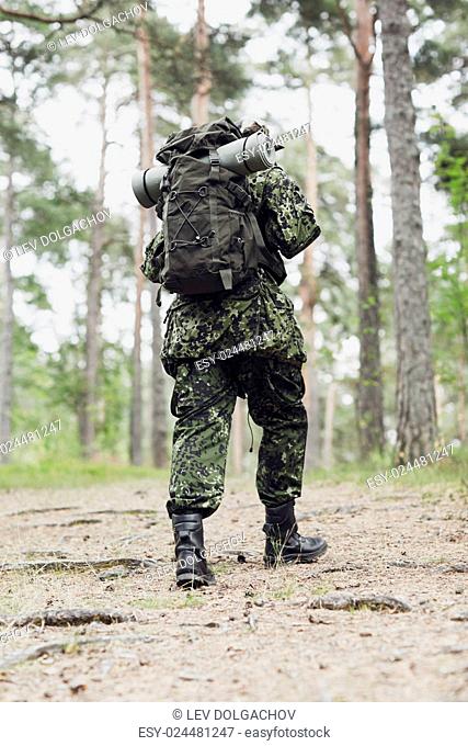 war, hiking, army and people concept - young soldier, ranger or hunter with backpack walking in forest