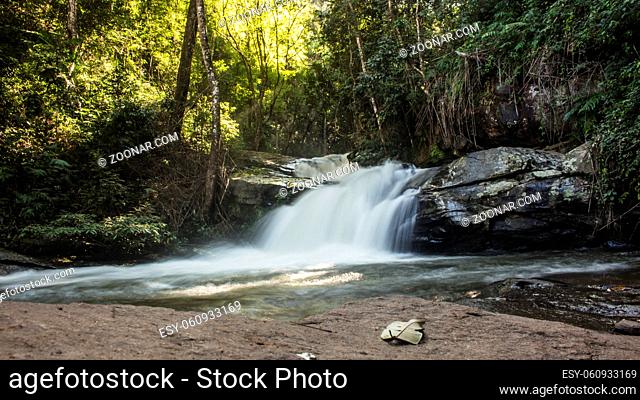 Horizontal photo of long exposure of adorable small waterfall surrounded by lush green foliage in Mae Klang Luang. Chiang Mai, Thailand