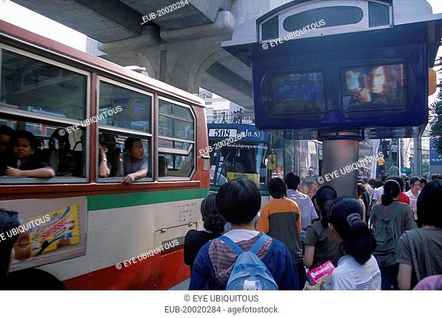 Bus and passengers at bus stop in Siam Square beside one video screen showing bus times and another a music video