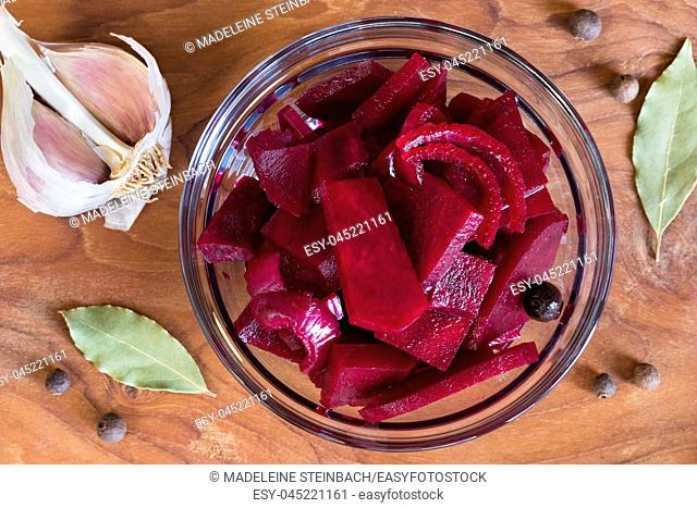 Fermented red beet with onions in a glass bowl, with garlic, allspice and bay leaf in the background, top view