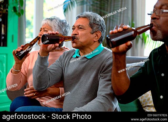 Two diverse senior couple and their african american male friend watching tv and drinking beer