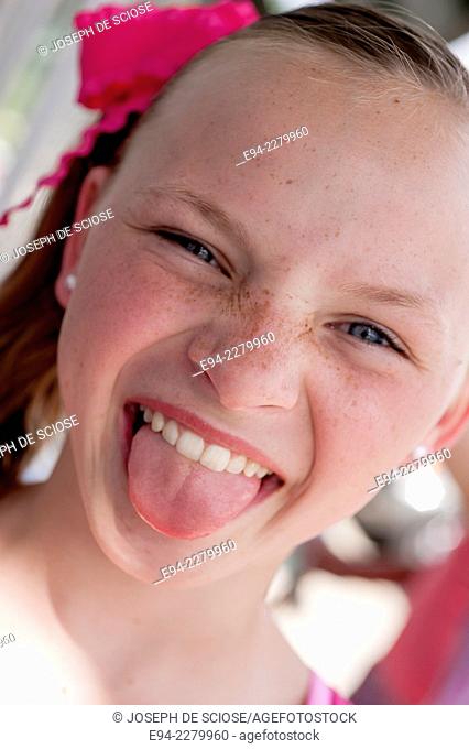 Portrait of a 10 year old girl with freckles sticking her tongue out at the camera making a funny face