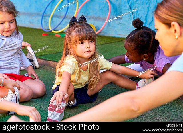 Kleines Mädchen beim Dehnen im Sportunterricht mit anderen Kindern in der Kindertagesstätte