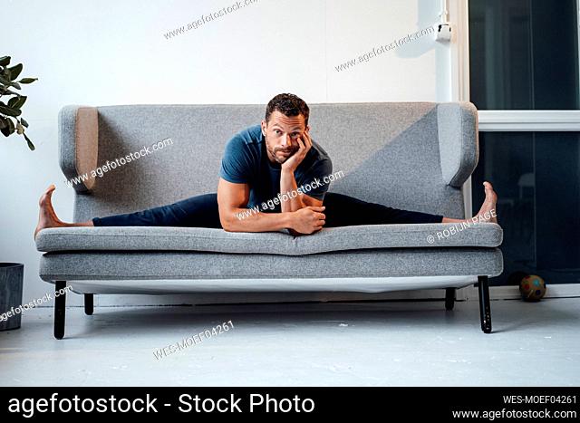 Mature man exercising with legs apart on sofa at home