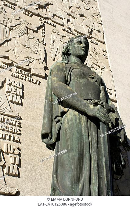 There is a bronze sculpture of a woman with sword against a wall of stone carving on the Palacio de Justica court on Campo dos Martires da Patria