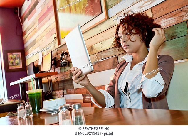 Mixed race woman using tablet computer in cafe