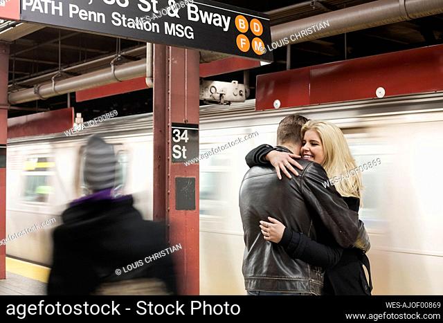 Girlfriend smiling while embracing boyfriend standing at subway station