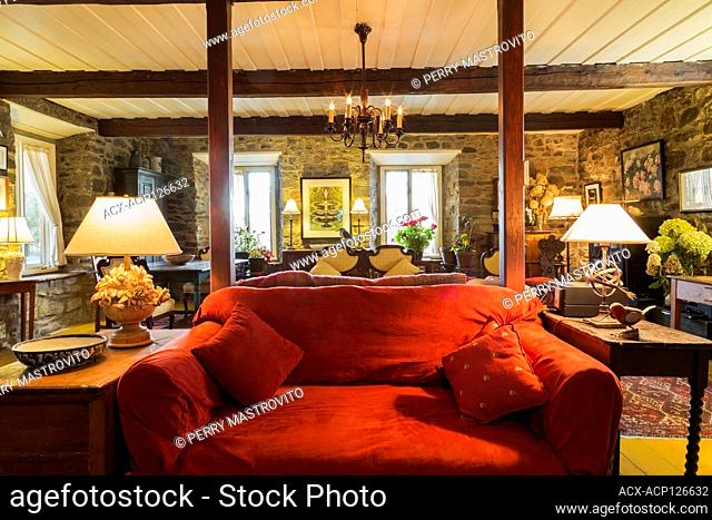 Red upholstered loveseat and antique furniture in living room inside an old renovated 1650s house, Quebec, Canada. This image is property released