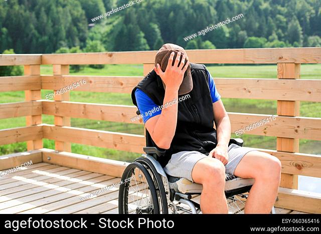 Disabled young man on a wheelchair in nature feeling depressed, lonely and sad