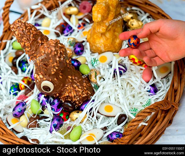 hands of a child unwrap a chocolate candy egg with a large Easter egg basket in the background during Easter celebrations with family and relatives